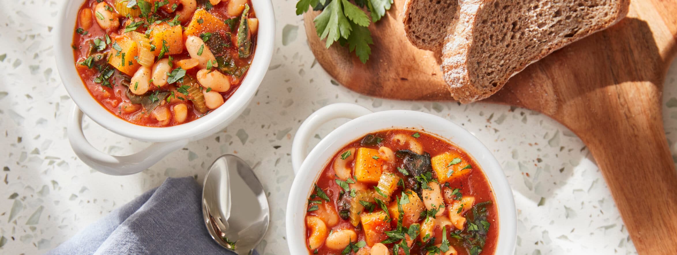 Two bowls of Pasta Fagioli sitting next to dark rye bread