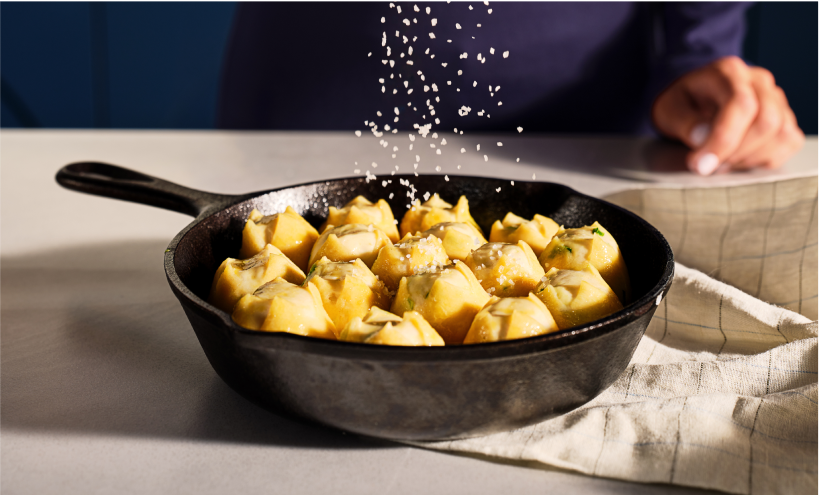 A sprinkle of salt faling over a pan of dumplings in a cast iron pan.