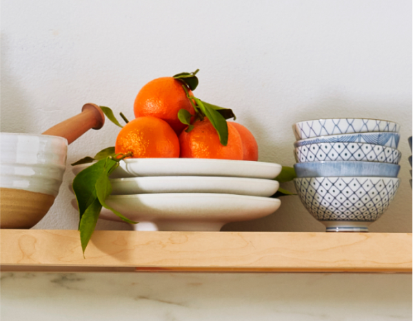 A series of white and blue dishes on open shelving with a stack of tangerines on top.