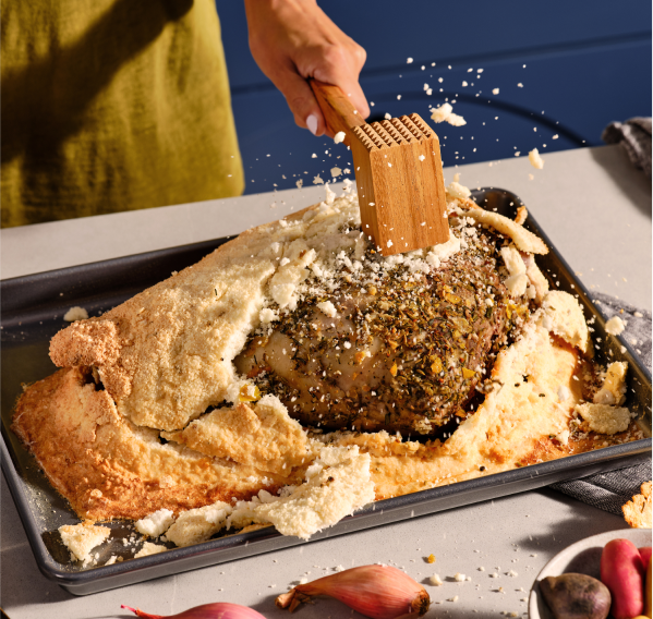 A person using a wooden mallet to crack open a salt crusted roast.