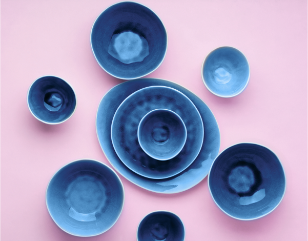 A series of blue ceramic bowls stacked inside eachother and arranged on a light pink-purple background.