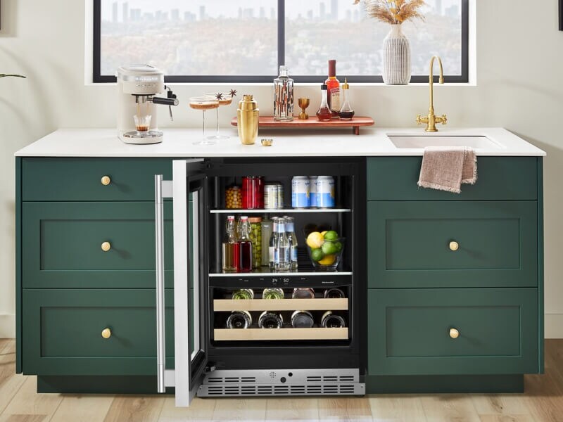 An open beverage center surrounded by teal cabinetry