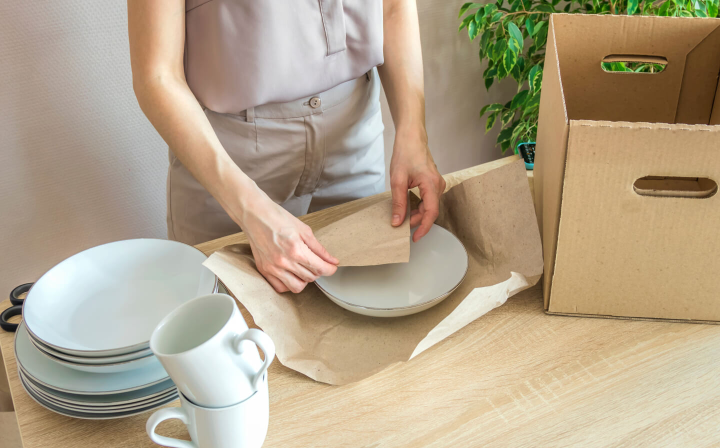 Person wrapping dishes in paper packaging wrap Person wrapping dishes in paper packaging wrap