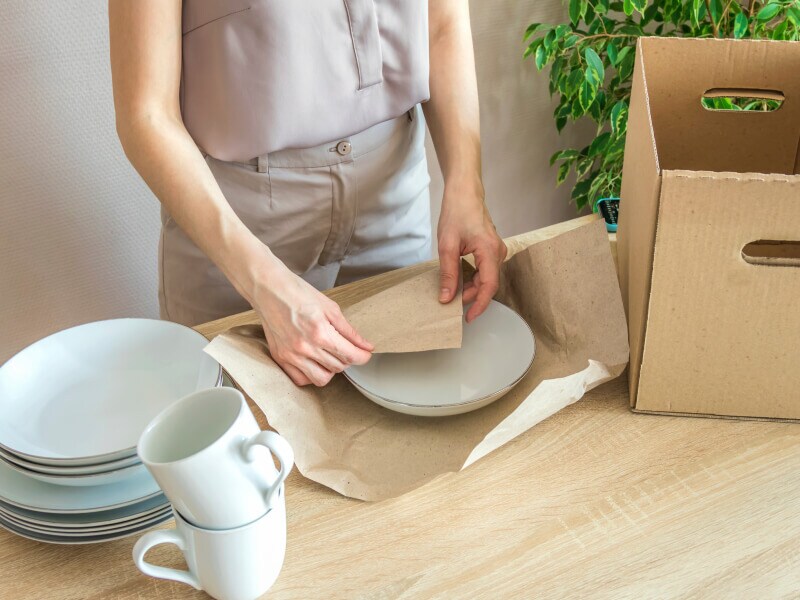 Person wrapping dishes in paper packaging wrap Person wrapping dishes in paper packaging wrap