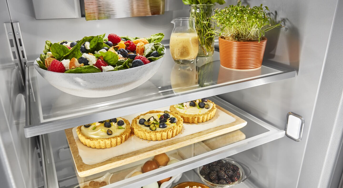 An open refrigerator with fruit tarts on one shelf