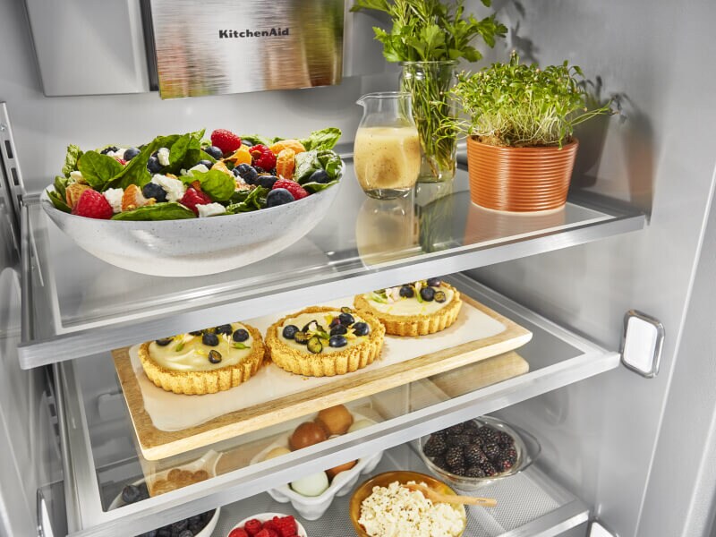 An open refrigerator with fruit tarts on one shelf