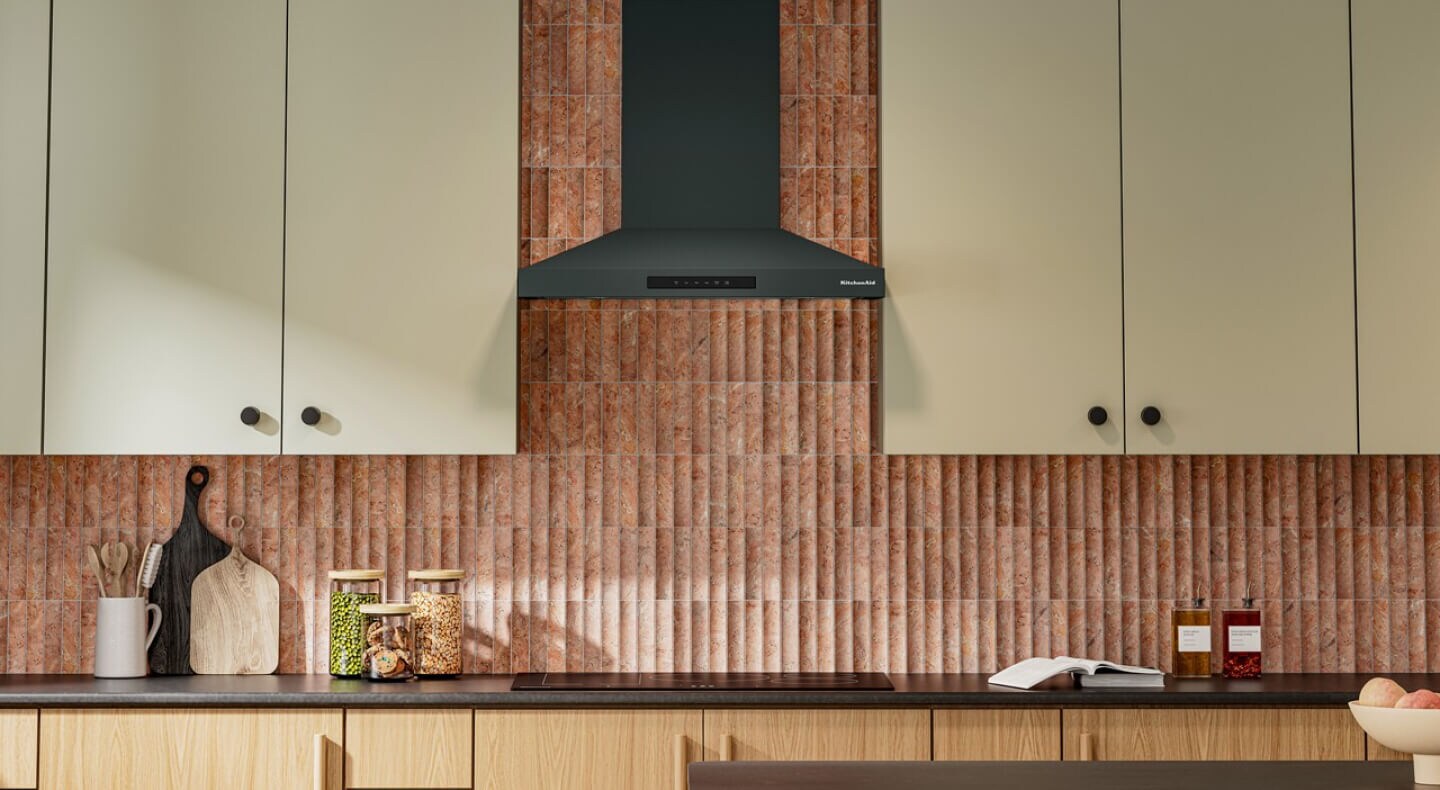 Juniper KitchenAid® range hood in front of a brick-style backsplash with cream-colored cabinetry