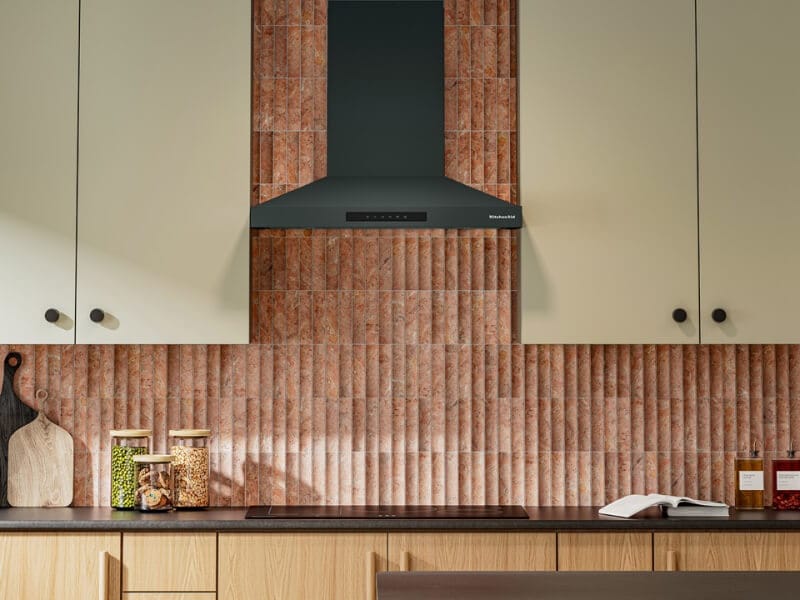 Juniper KitchenAid® range hood in front of a brick-style backsplash with cream-colored cabinetry