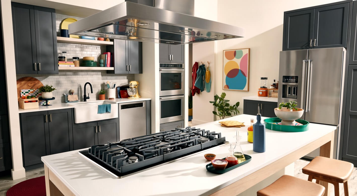 Suite of KitchenAid® stainless steel appliances, including a gas cooktop and island canopy range hood