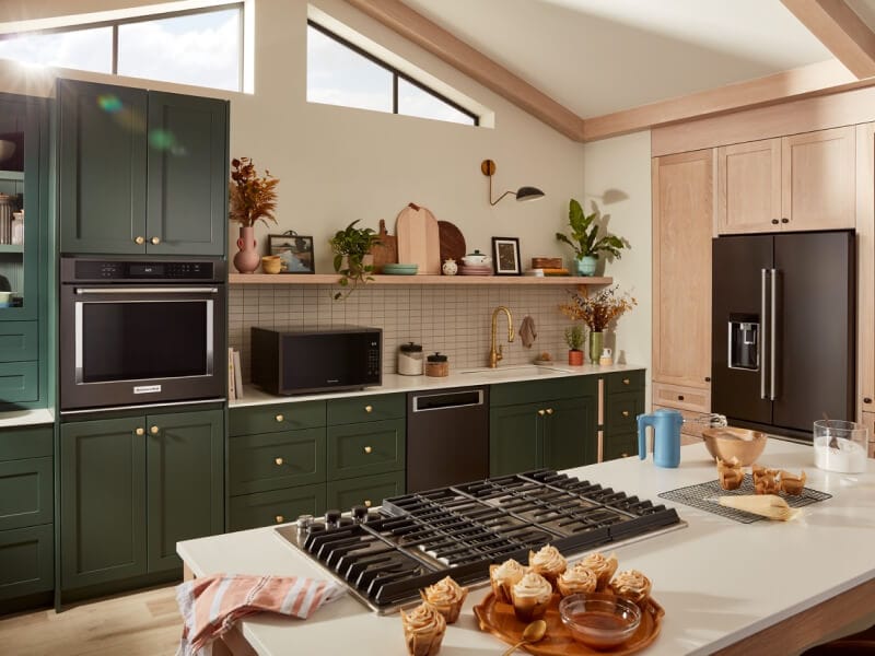 Suite of KitchenAid® black stainless steel appliances in dark green cabinetry