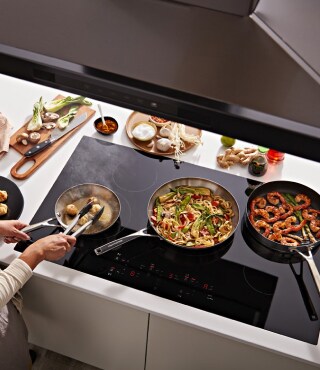A person cooking on a KitchenAid® cooktop