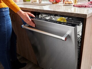 A hand closing a KitchenAid® top control dishwasher