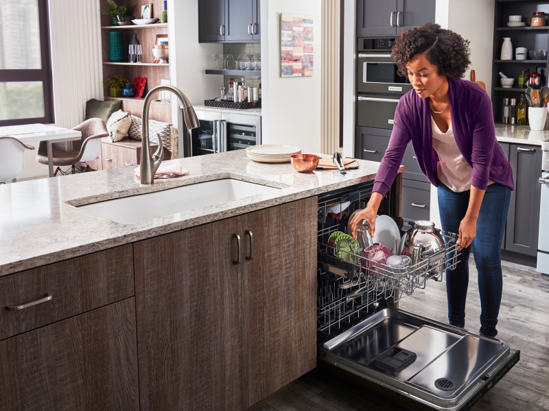 A woman loading a glass onto the top rack of an open dishwasher