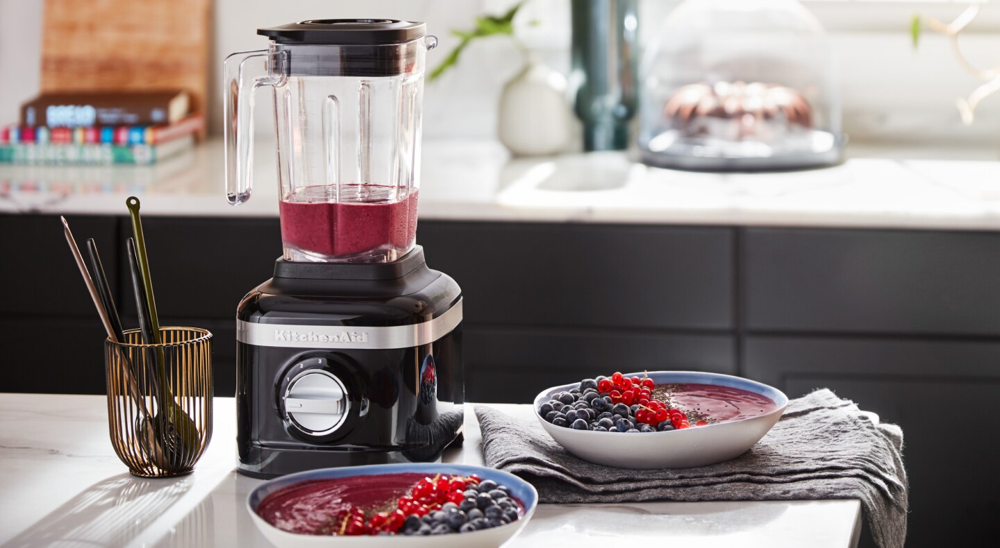 Black KitchenAid® blender next to two smoothie bowls garnished with fresh fruit