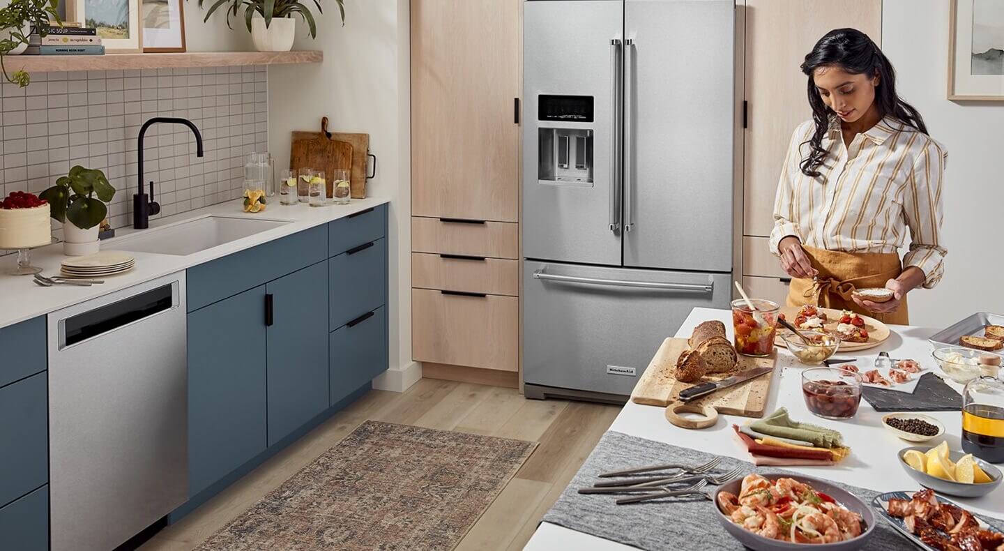 Person prepping food on a kitchen island in front of French door refrigerator Person prepping food on a kitchen island in front of French door refrigerator