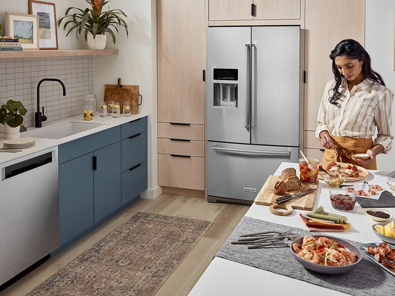 Person prepping food on a kitchen island in front of French door refrigerator Person prepping food on a kitchen island in front of French door refrigerator