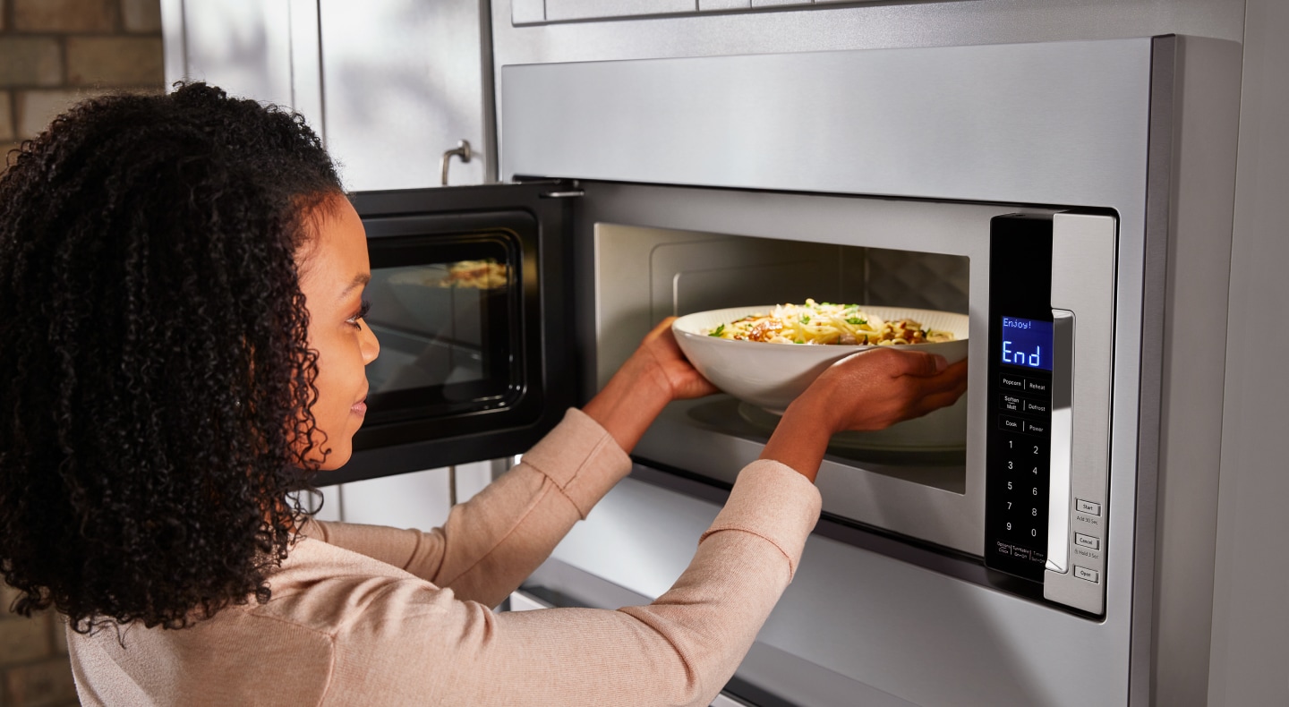 A person placing a dish in an open KitchenAid® microwave A person placing a dish in an open KitchenAid® microwave