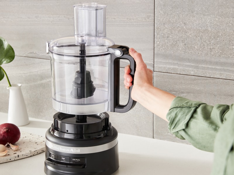 A woman attaching a KitchenAid® food processor bowl to the base of the appliance.