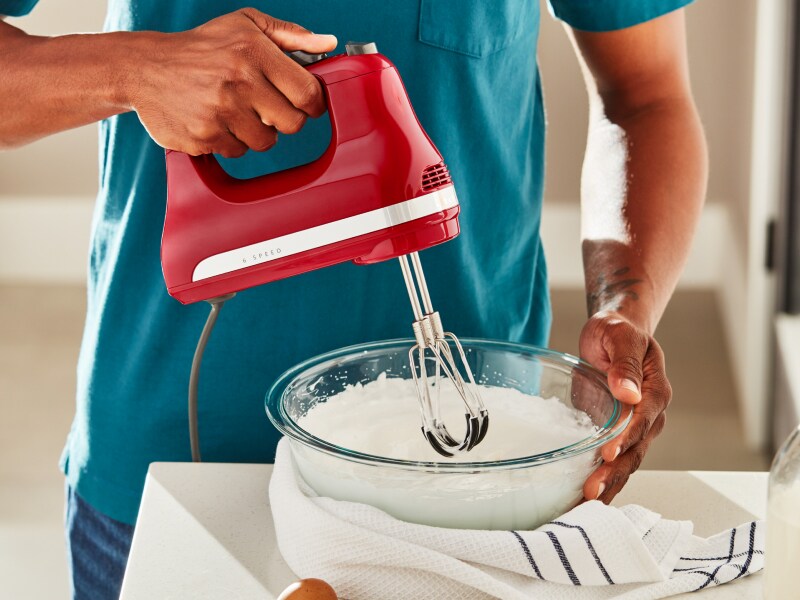 A man using a KitchenAid® hand mixer to whip egg whites. 