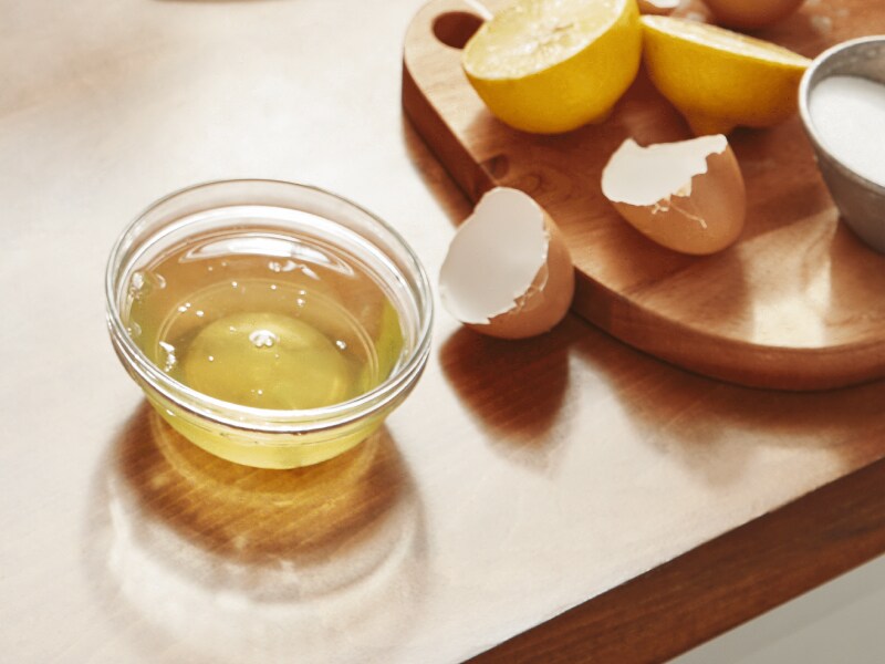 Egg whites in a bowl next to a cracked egg.