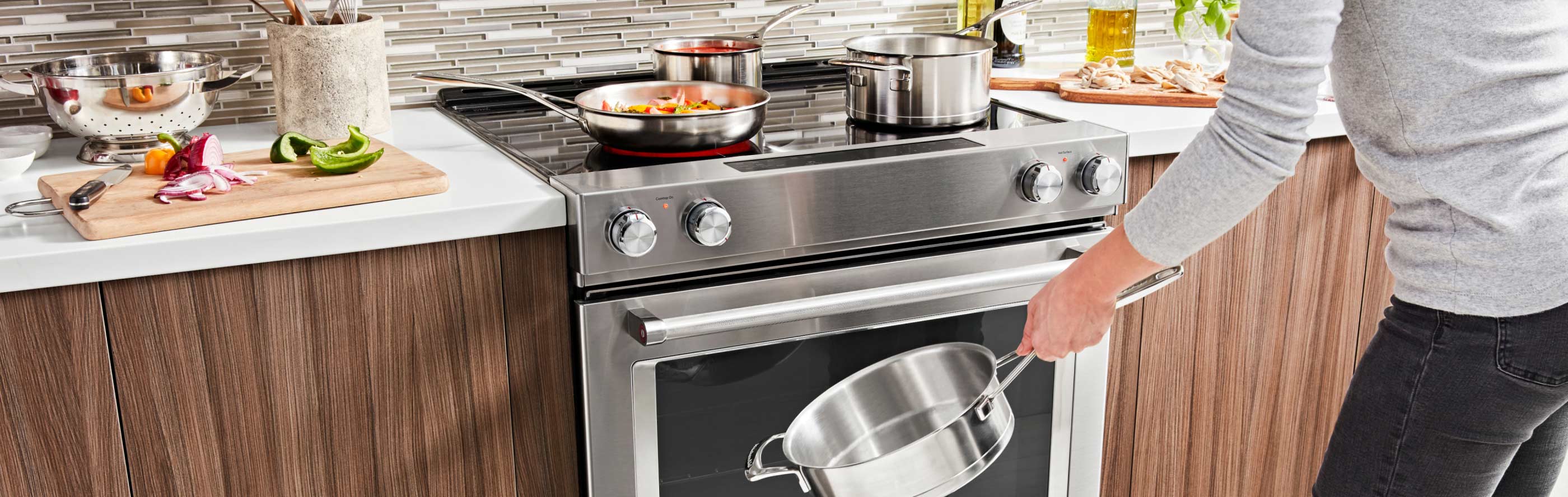 A person holding a pot in front of a KitchenAid® slide-in range