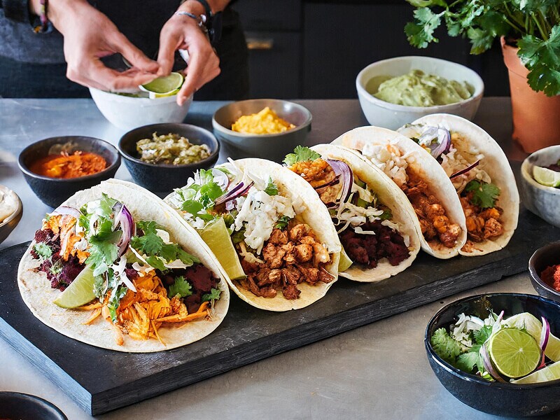 A row of tacos and various toppings