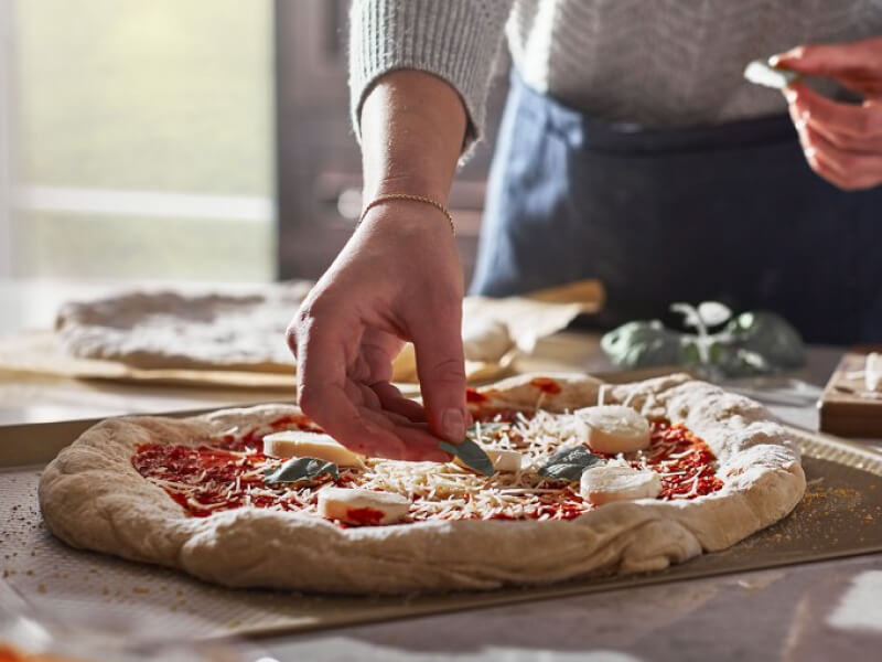 A person putting toppings on a pizza