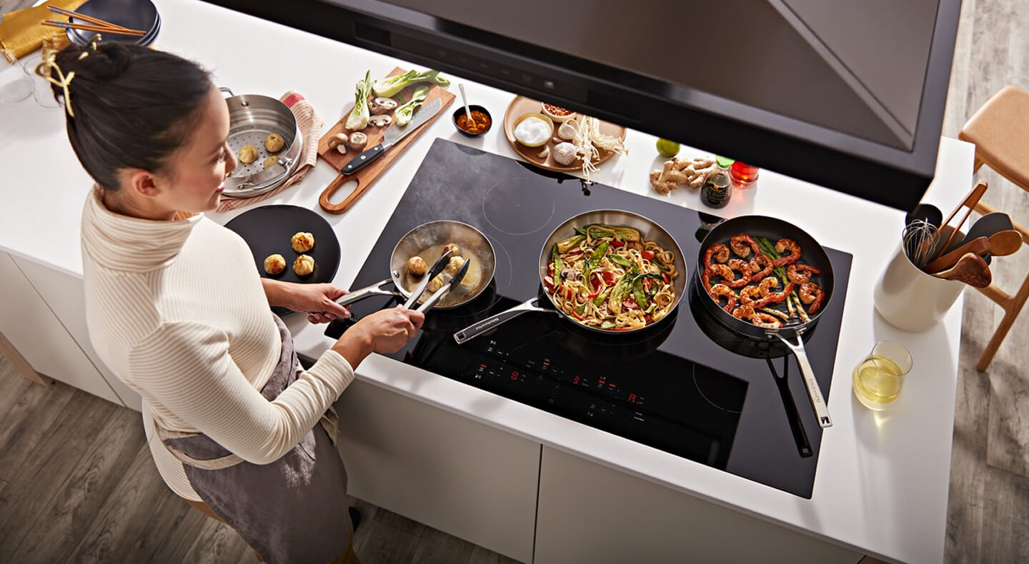 A person cooking several dishes on their cooktop