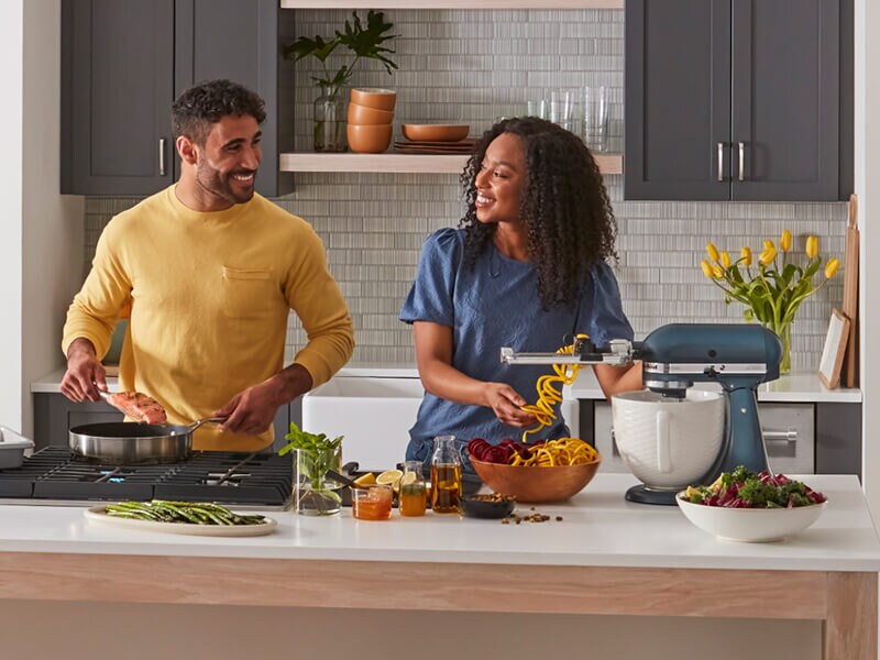 A man and woman cooking together and smiling at each other