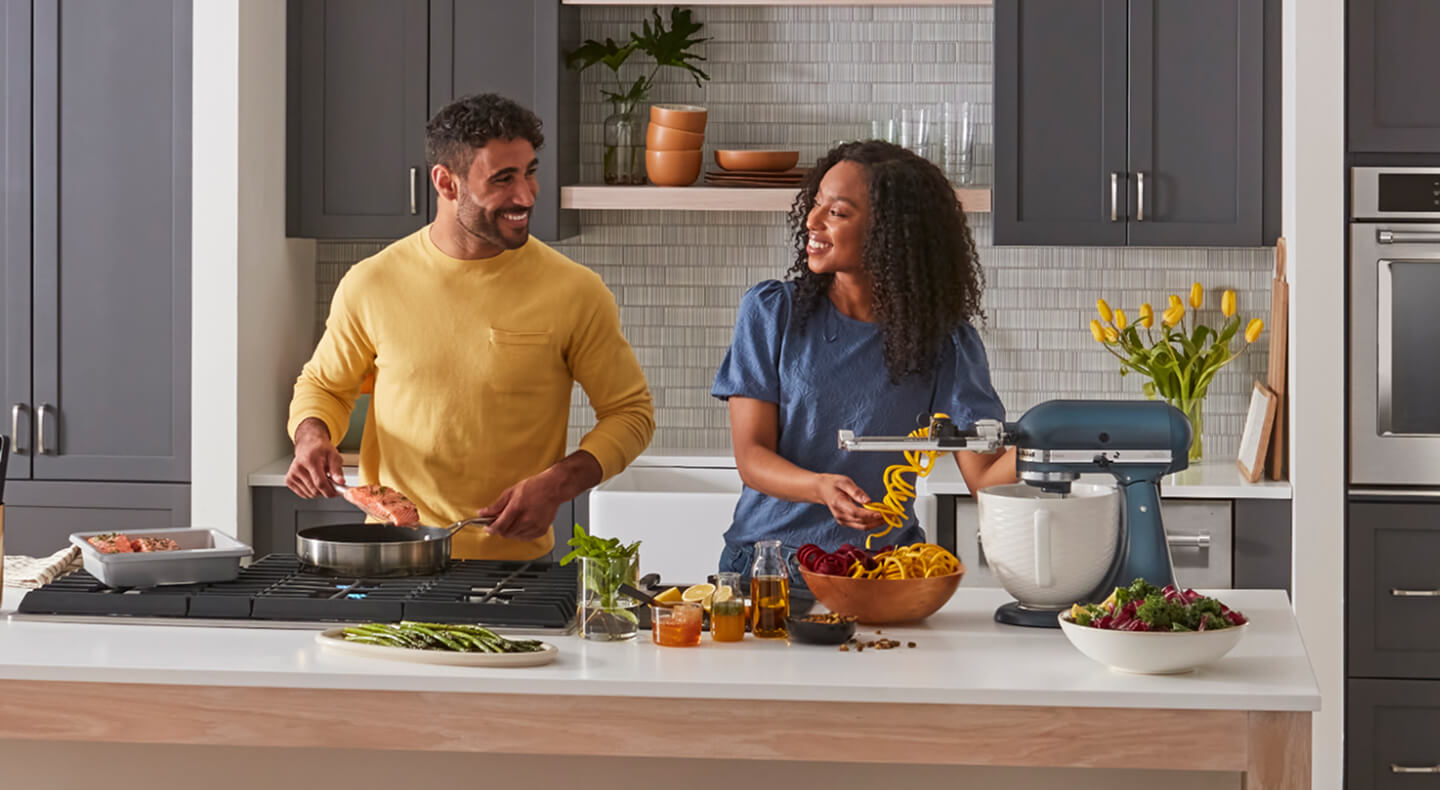 A man and woman cooking together and smiling at each other