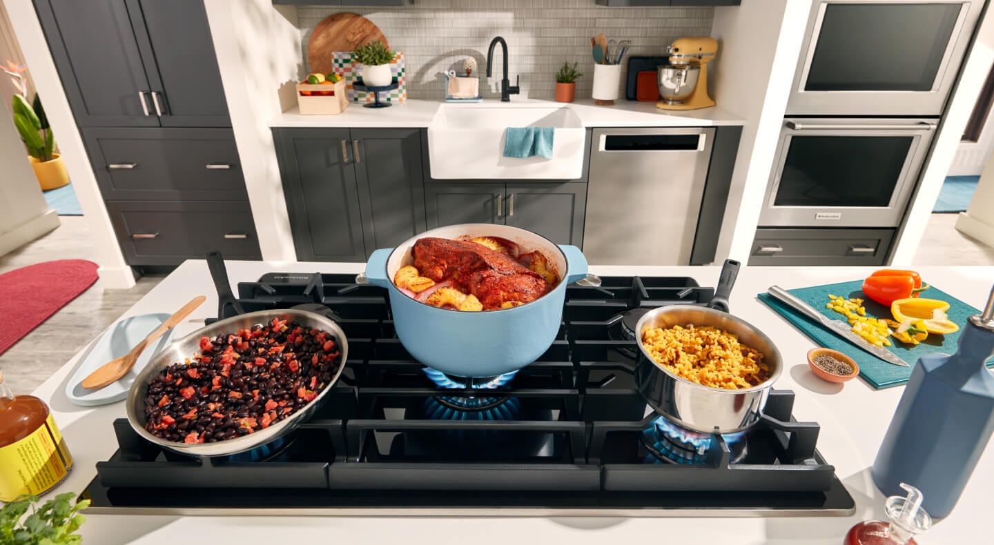 Dishes cooking in stock pots and a wok above the open flame of a gas cooktop Dishes cooking in stock pots and a wok above the open flame of a gas cooktop