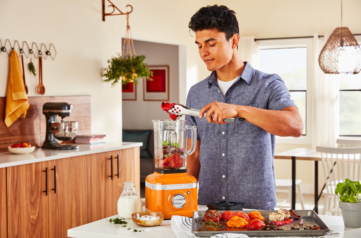 A man adding roasted vegetables to a KitchenAid® blender in a modern kitchen. A man adding roasted vegetables to a KitchenAid® blender in a modern kitchen.