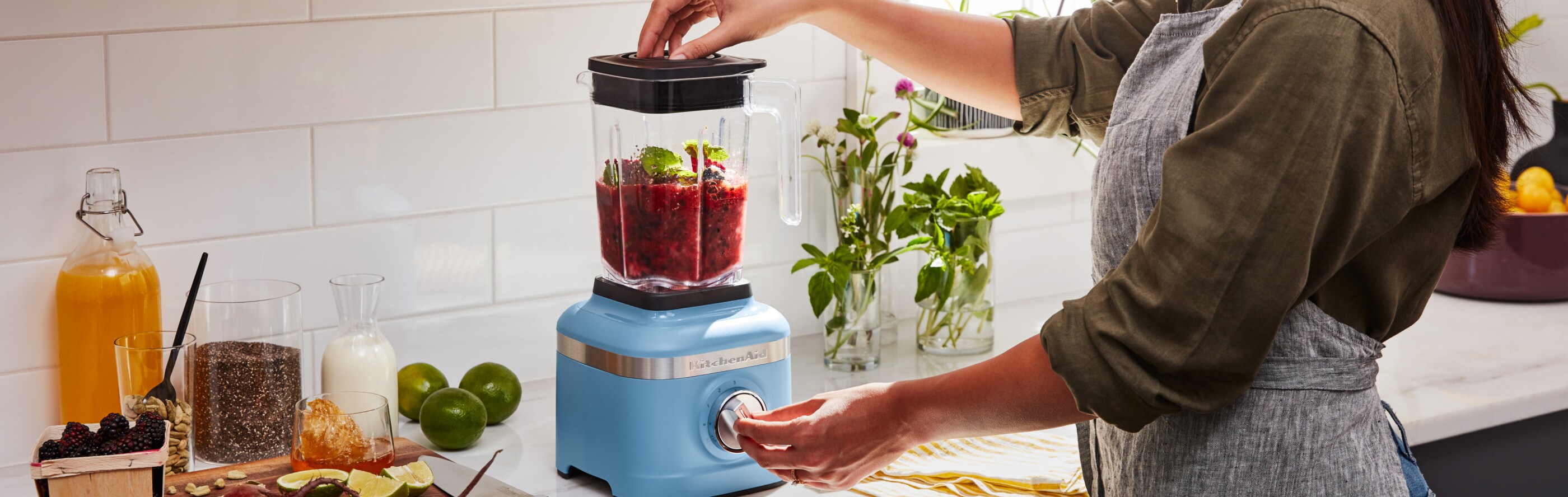 A woman blending fresh vegetables in a KitchenAid® blender in a modern kitchen.