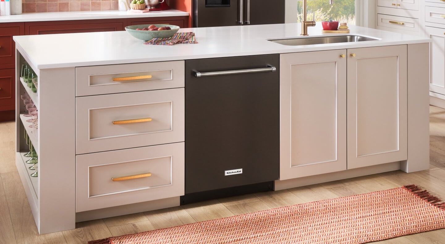 A KitchenAid® built-in top control dishwasher with a towel bar handle placed in a kitchen island with cream cabinets and a white countertop