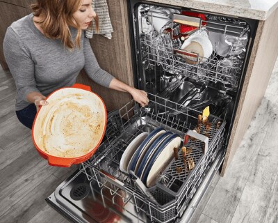 Person kneeling and filling dishwasher bottom rack