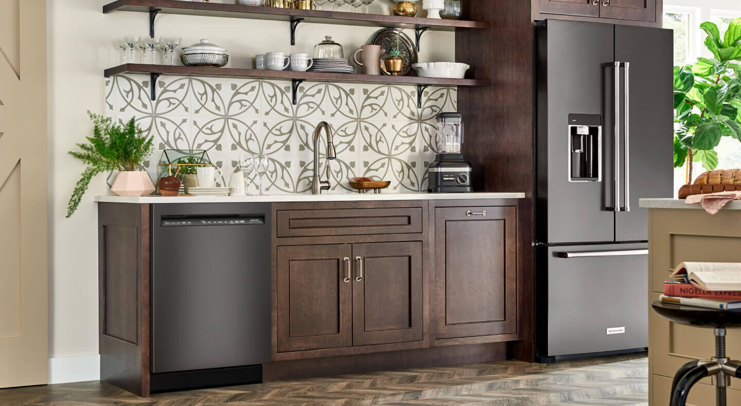 A black built-in front control dishwasher in a kitchen with brown cabinets and shelving and a black KitchenAid® refrigerator