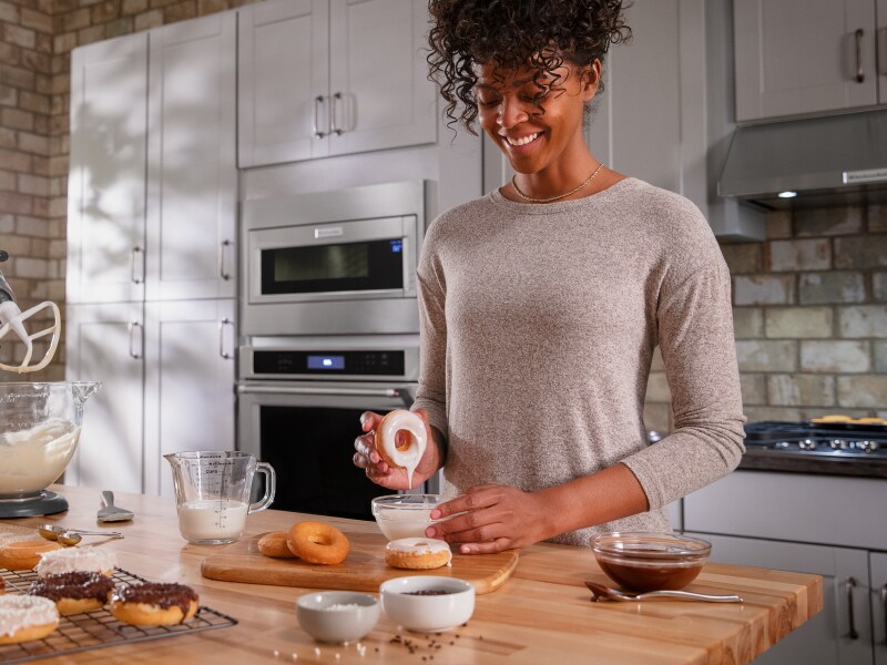 Person dipping a donut in homemade frosting Person dipping a donut in homemade frosting