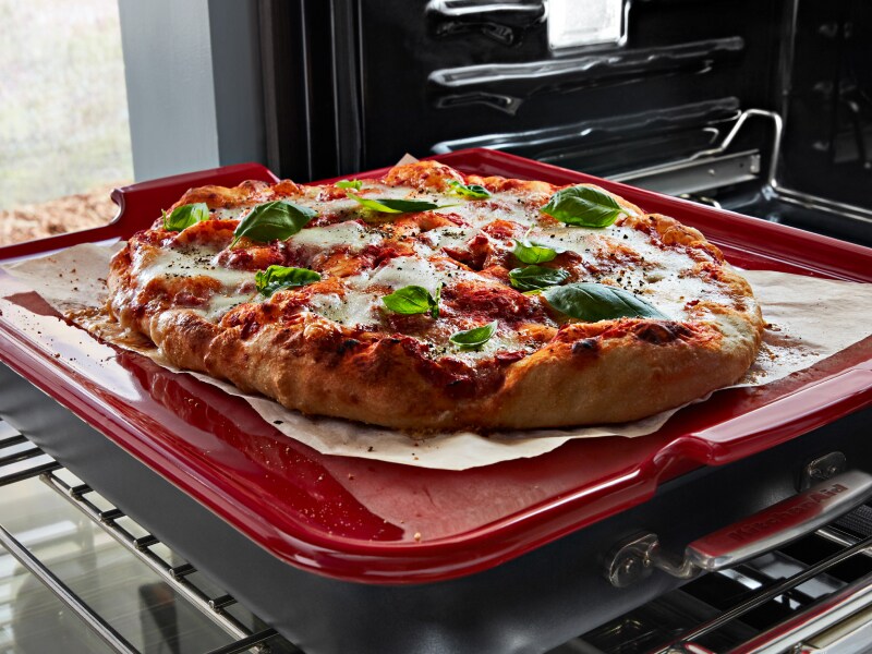  A pizza topped with fresh vegetables on a red baking stone