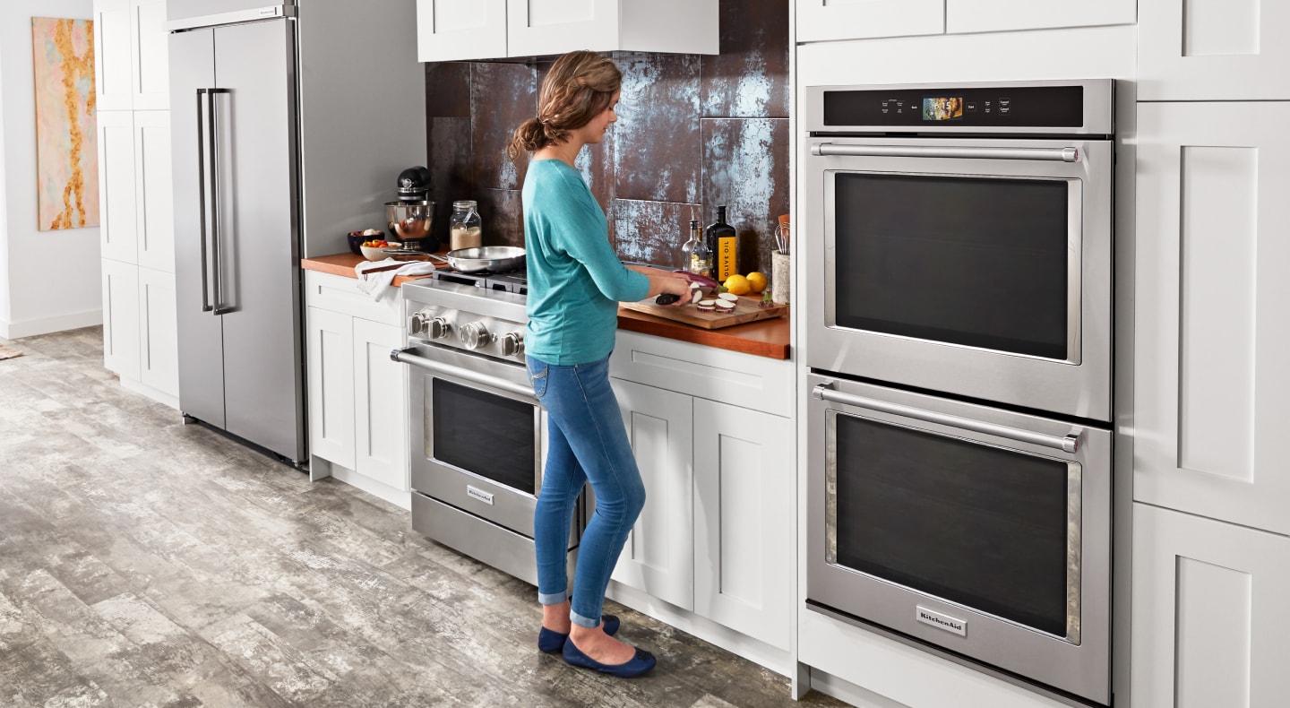 A woman chopping vegetables next to a KitchenAid® double wall oven A woman chopping vegetables next to a KitchenAid® double wall oven