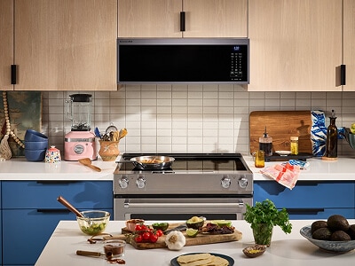 A galley kitchen with blue lower cabinets and light wood upper cabinets against the wall side, and an island with white countertops on the other side