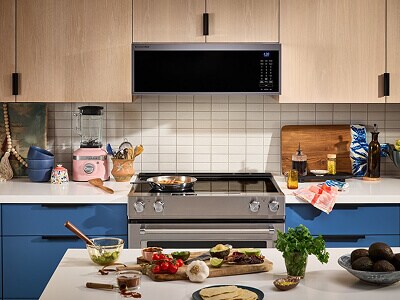 A galley kitchen with blue lower cabinets and light wood upper cabinets against the wall side, and an island with white countertops on the other side