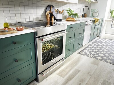A long row of dark green cabinetry with stainless steel appliances, white countertops and white tile backsplash