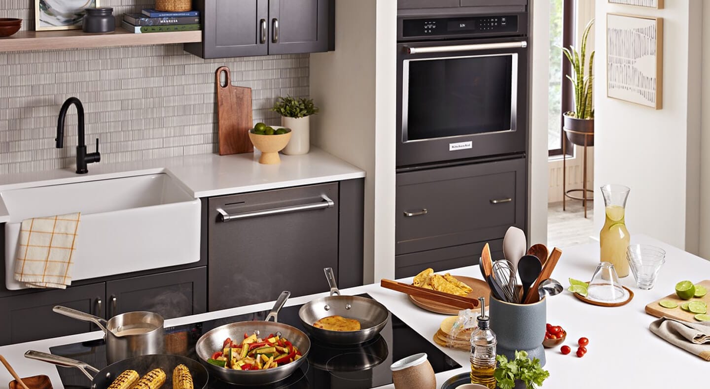 A galley kitchen with dark brown cabinetry, white countertops, a sink and built-in oven on one side, and an island with white countertops and a stovetop on the other A galley kitchen with dark brown cabinetry, white countertops, a sink and built-in oven on one side, and an island with white countertops and a stovetop on the other