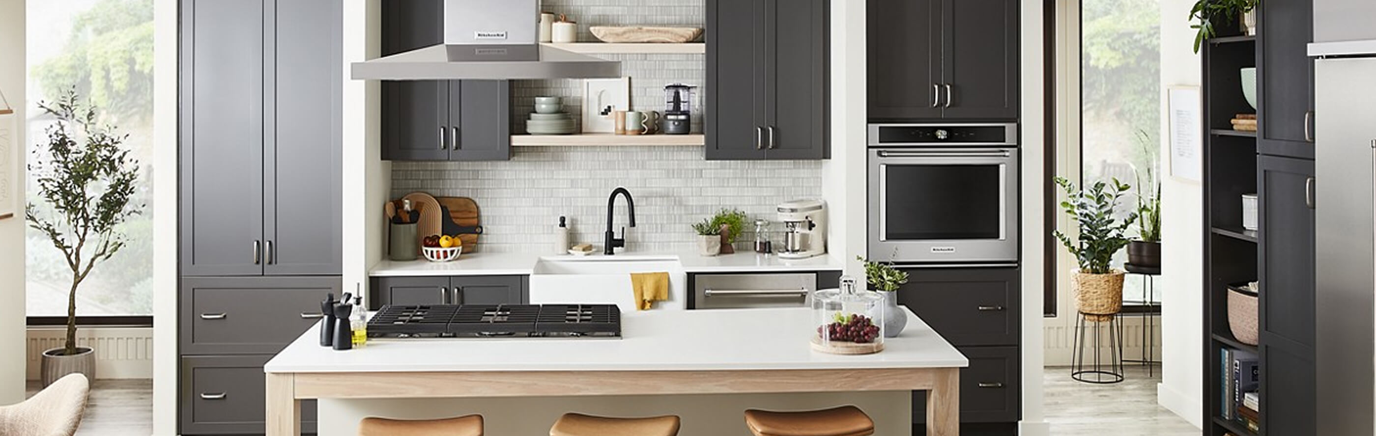 A long and narrow kitchen with brown cabinets and white cabinets against the wall with a white island in the middle of the room