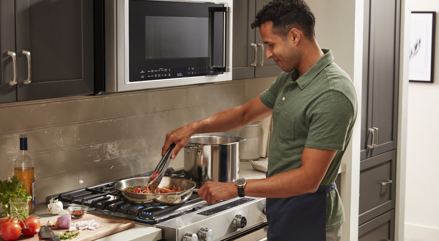 Person stirring a pasta dish on a KitchenAid® stovetop