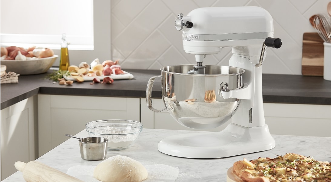 A white KitchenAid® stand mixer next to a pizza