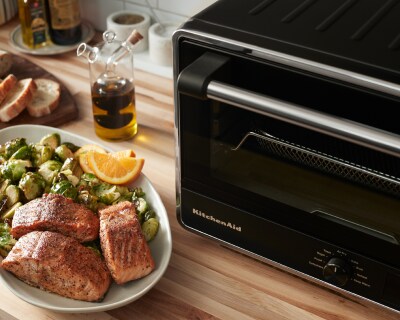 Salmon on a plate with Brussels sprouts and orange wedges next to a KitchenAid® countertop oven