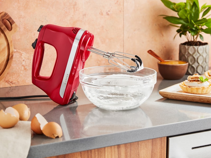 KitchenAid® hand mixer next to an empty mixing bowl of whipped egg whites and meringue tarts. KitchenAid® hand mixer next to an empty mixing bowl of whipped egg whites and meringue tarts.