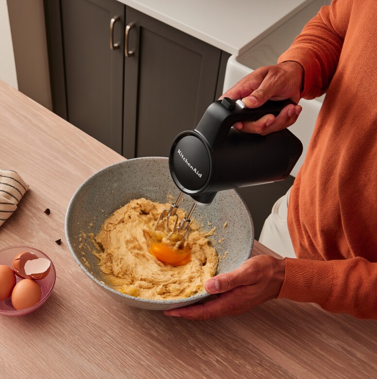 A person using a KitchenAid Go™ Hand Mixer to mix in eggs to batter.