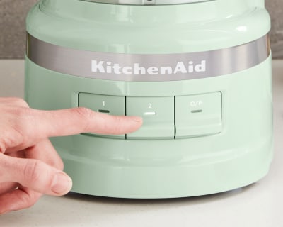 A person selecting a setting on a green KitchenAid® food processor